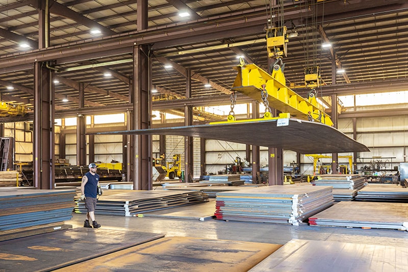 A warehouse employee moves steel plate using a crane